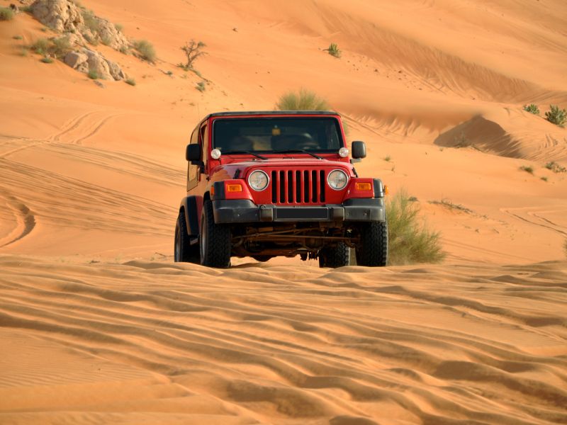 Roter Jeep heizt durch den Sand der Wüste Dubais
